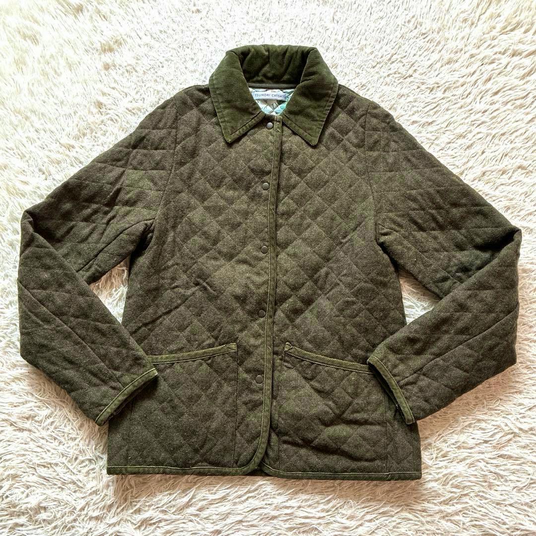 A green quilted tsumori chisato men's polyester jacket laid flat showing the front, collar, snap buttons, and pockets.