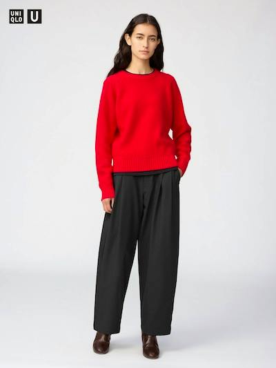 Model wearing the black tuck barrel-leg pants shown full length with a red sweater and brown shoes.