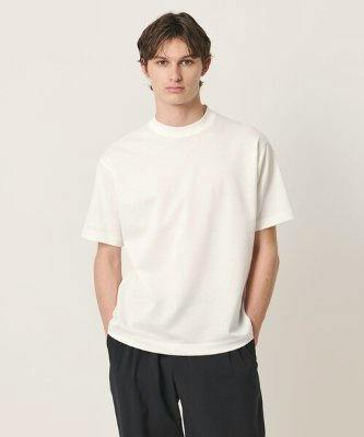 A model wearing a white Tuck Jersey T-shirt and dark pants standing against a neutral light background.