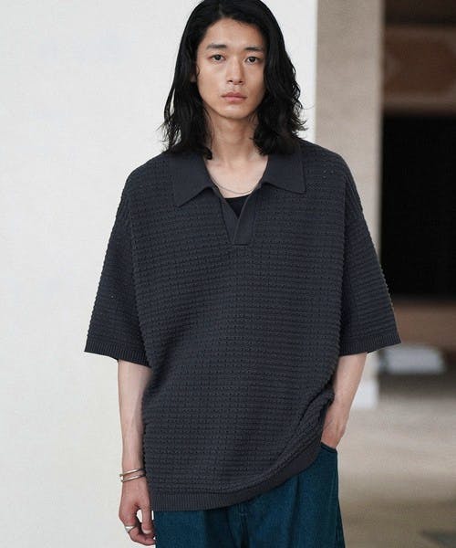 A model wearing a dark tuck skipper knit polo shirt shown from the front.