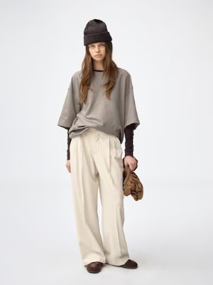 A model wearing the wide tuck women's pants in a light beige color.