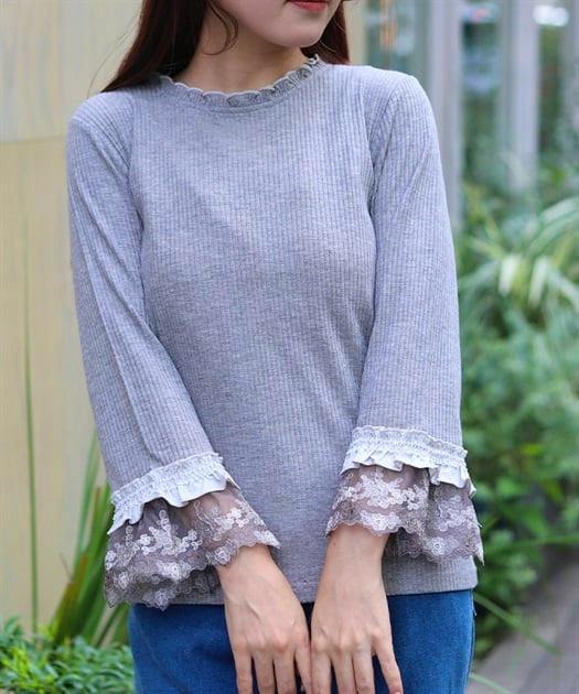 Model wearing a grey ribbed pullover blouse with tulle-embroidered lace cuffs and a frilled neckline.
