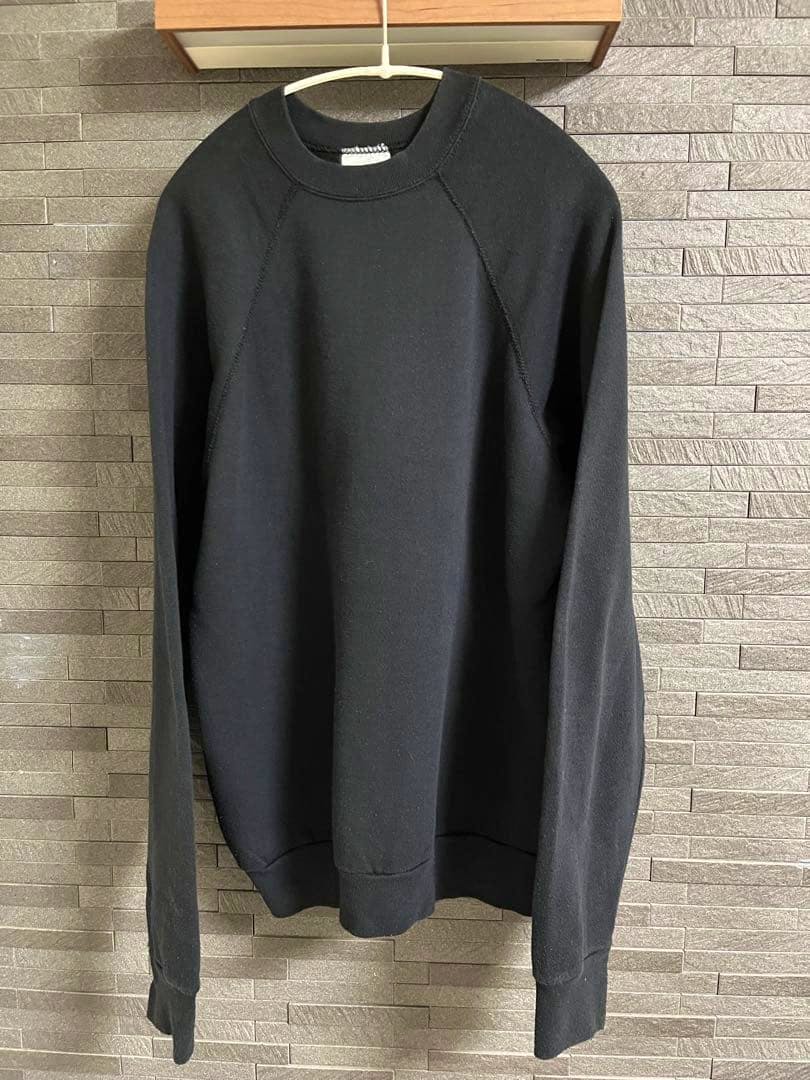 Plain black Tultex raglan sweatshirt hanging on a hanger against a tiled wall.