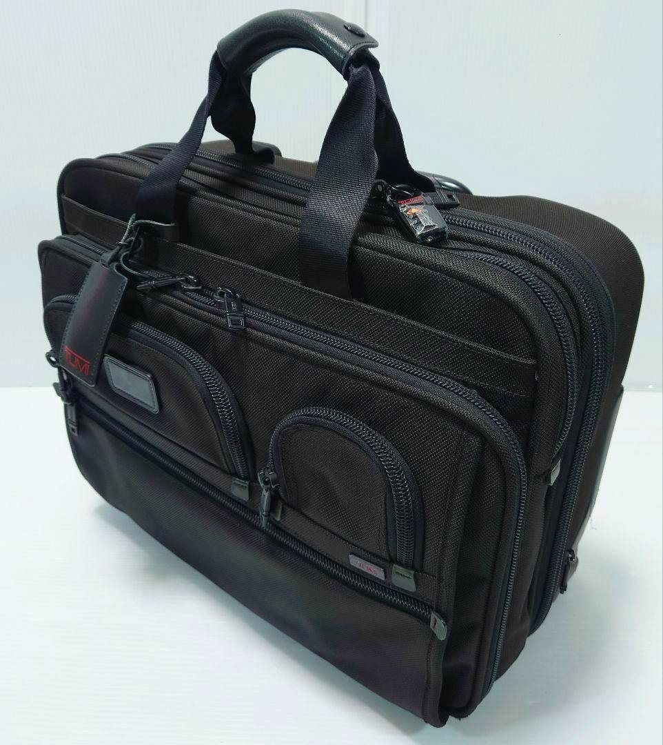 Black TUMI polyester briefcase-style bag shown at a three-quarter angle with multiple zippered compartments and top handles.