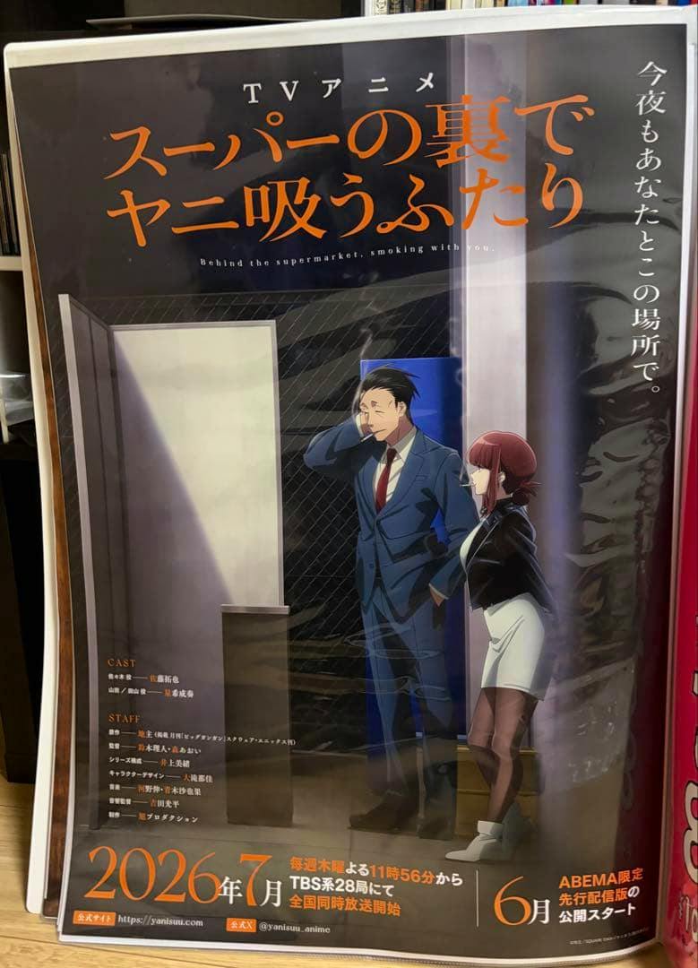 Photograph of a B2 announcement poster for the TV anime "スーパーの裏でヤニ吸うふたり" showing two characters standing by a doorway with the title in large orange text and broadcast information at the bottom.