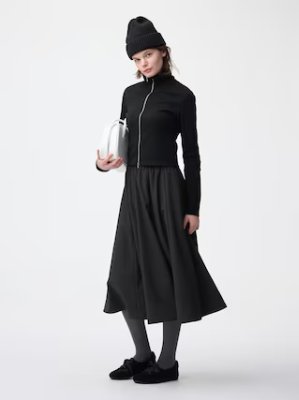 Model wearing a black zip-front cardigan paired with a black skirt on a white background.