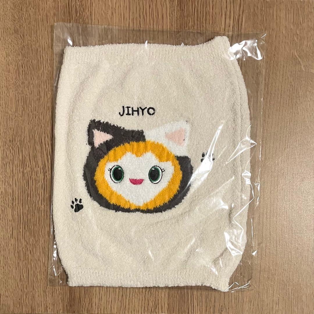 Cream polyester belly warmer in plastic packaging showing an embroidered mascot face and the text "JIHYO" on a wooden background.