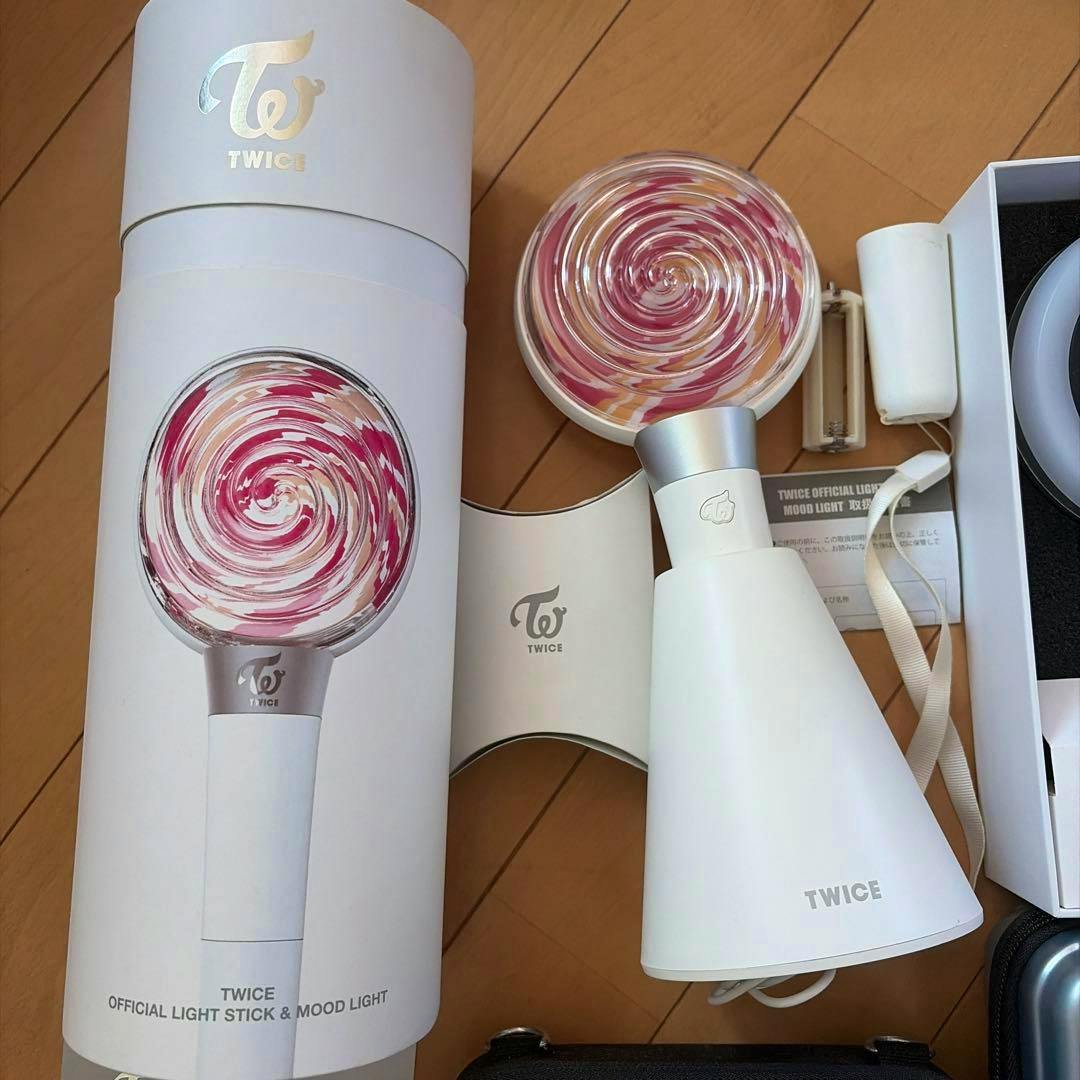 A TWICE penlight with its cylindrical packaging and cone-shaped stand displayed on a wooden floor.