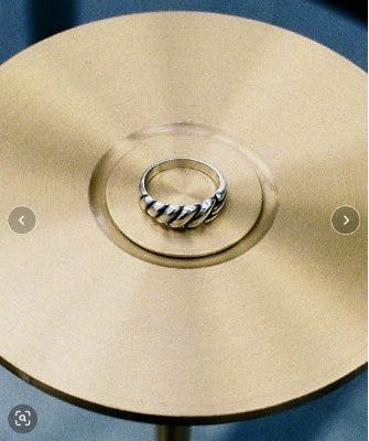 A twisted metal ring placed on a round gold-colored surface.