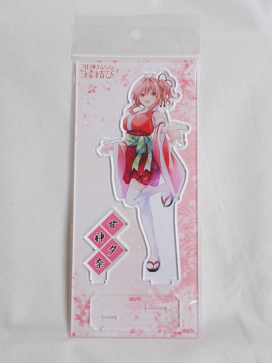 Packaged acrylic stand showing Yuna Amagami figure, the stand base, and a nameplate against pink backing.