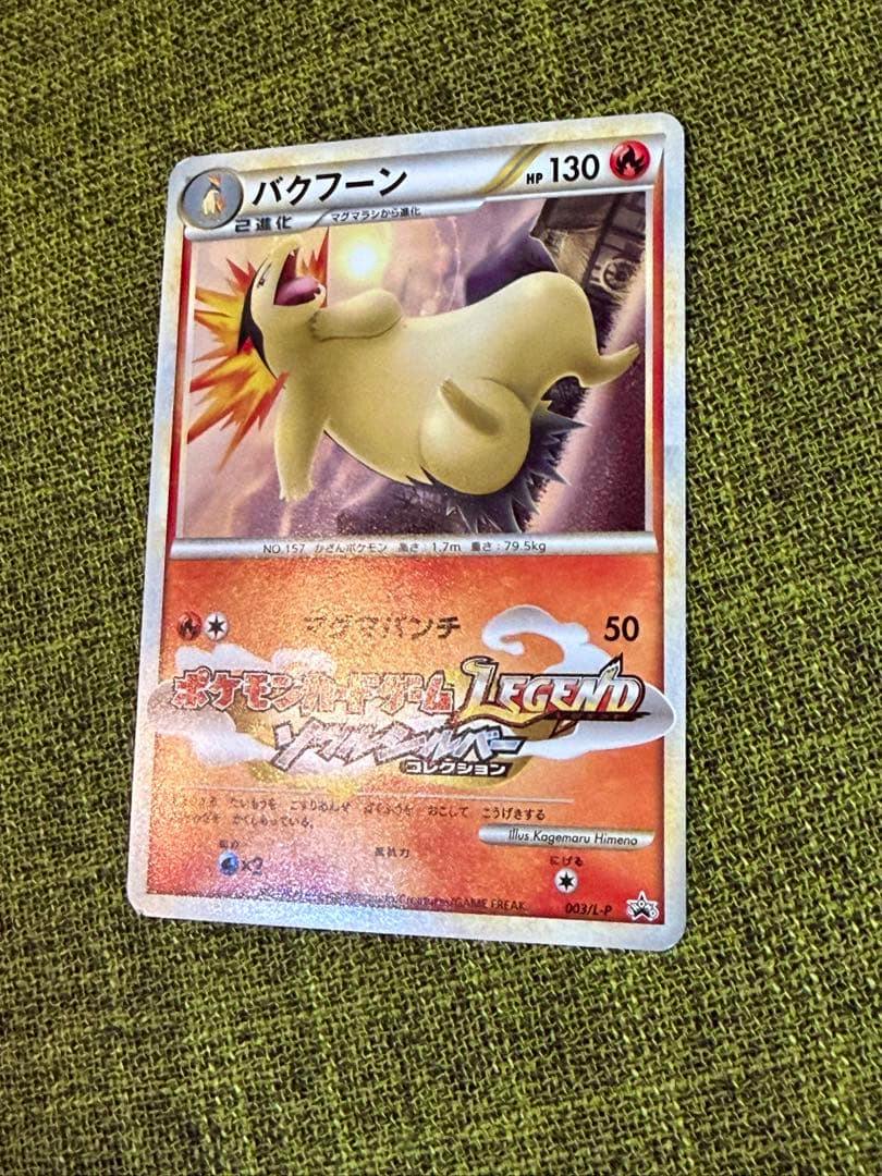 A photograph of the バクフーン trading card PROMO 003/L-P placed on green textured fabric.