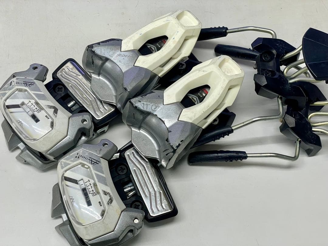 Top-down view of a pair of TYROLIA Attack 11 ski bindings in silver and white placed on a flat surface.