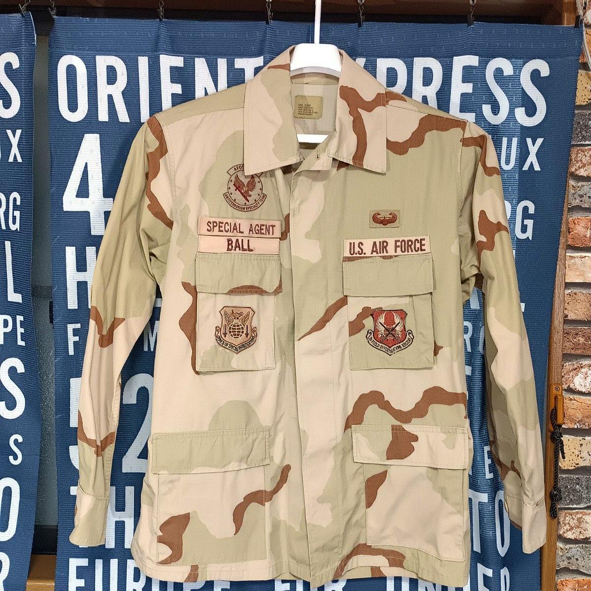 Front view of a U.S. Air Force 3-color desert camouflage BDU jacket with "SPECIAL AGENT" and "U.S. AIR FORCE" name tapes and embroidered patches hanging on a hanger.