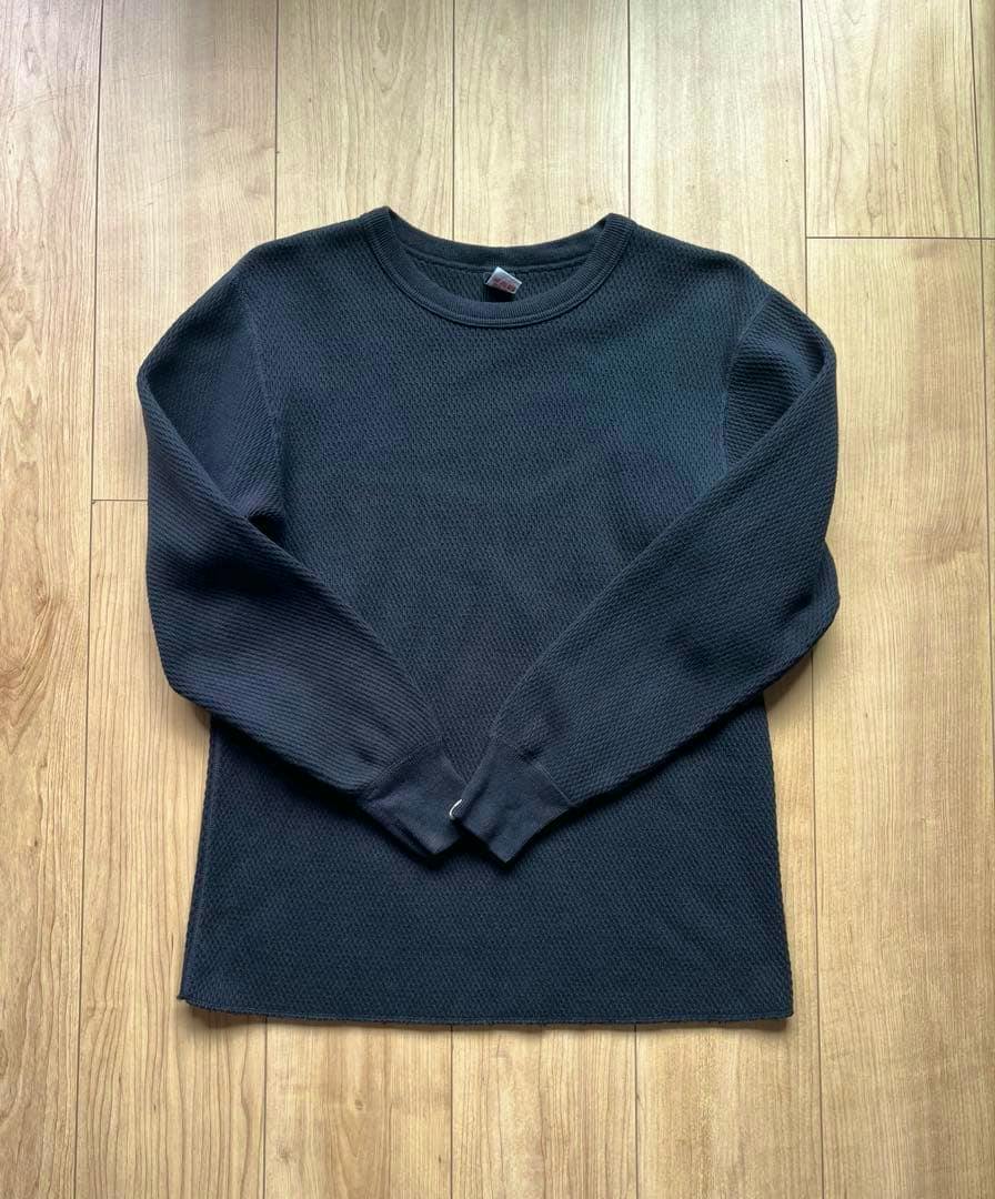 A dark waffle-knit thermal sweater laid flat on a wooden floor.