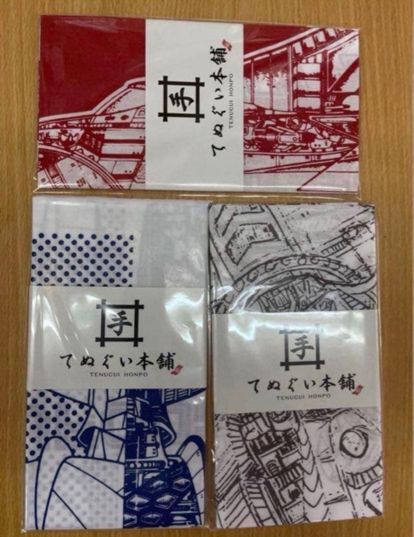 Three packaged cotton tenugui hand towels featuring UFO Robo Grendizer designs in red, blue, and gray, arranged on a wooden surface.