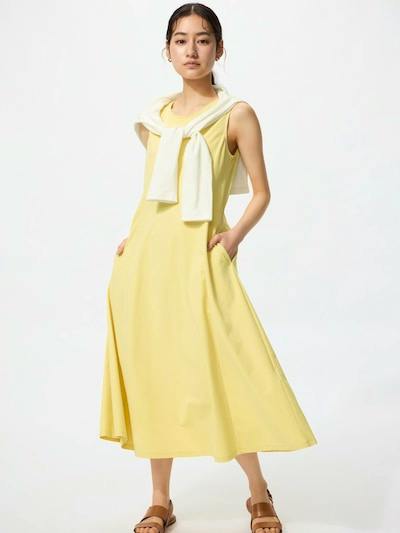 A model wearing a sleeveless, short-length yellow women's dress with a white sweater draped over the shoulders.