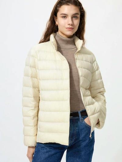 A model wearing a light beige full-zip men's nylon puffer jacket with horizontal quilting and hands in pockets.