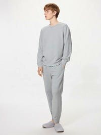A model wearing a light gray sweatshirt and matching sweatpants standing against a white background.