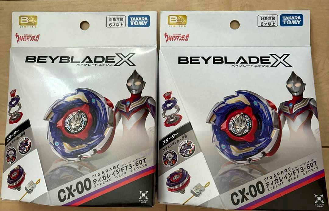 Front view of two boxed BEYBLADE X CX-00 (TIGARAGE/ティガレイジFT3-60T) packages showing the beyblade artwork and an Ultraman illustration.