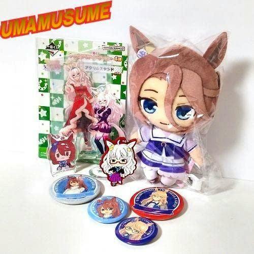 Assorted Uma Musume merchandise including a plush in plastic, several character can badges, and acrylic stands on a white background.