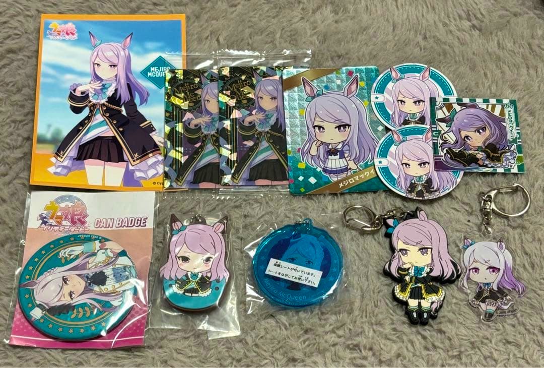 A collection of Mejiro McQueen rubber keychains, badges, and stickers arranged on a gray carpet.