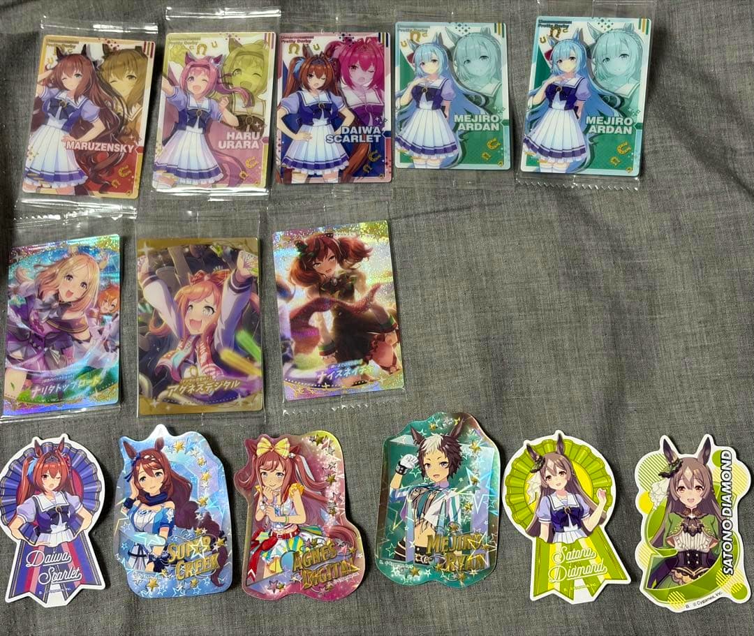 Multiple Uma Musume wafer cards and character stickers laid out on a gray fabric surface.