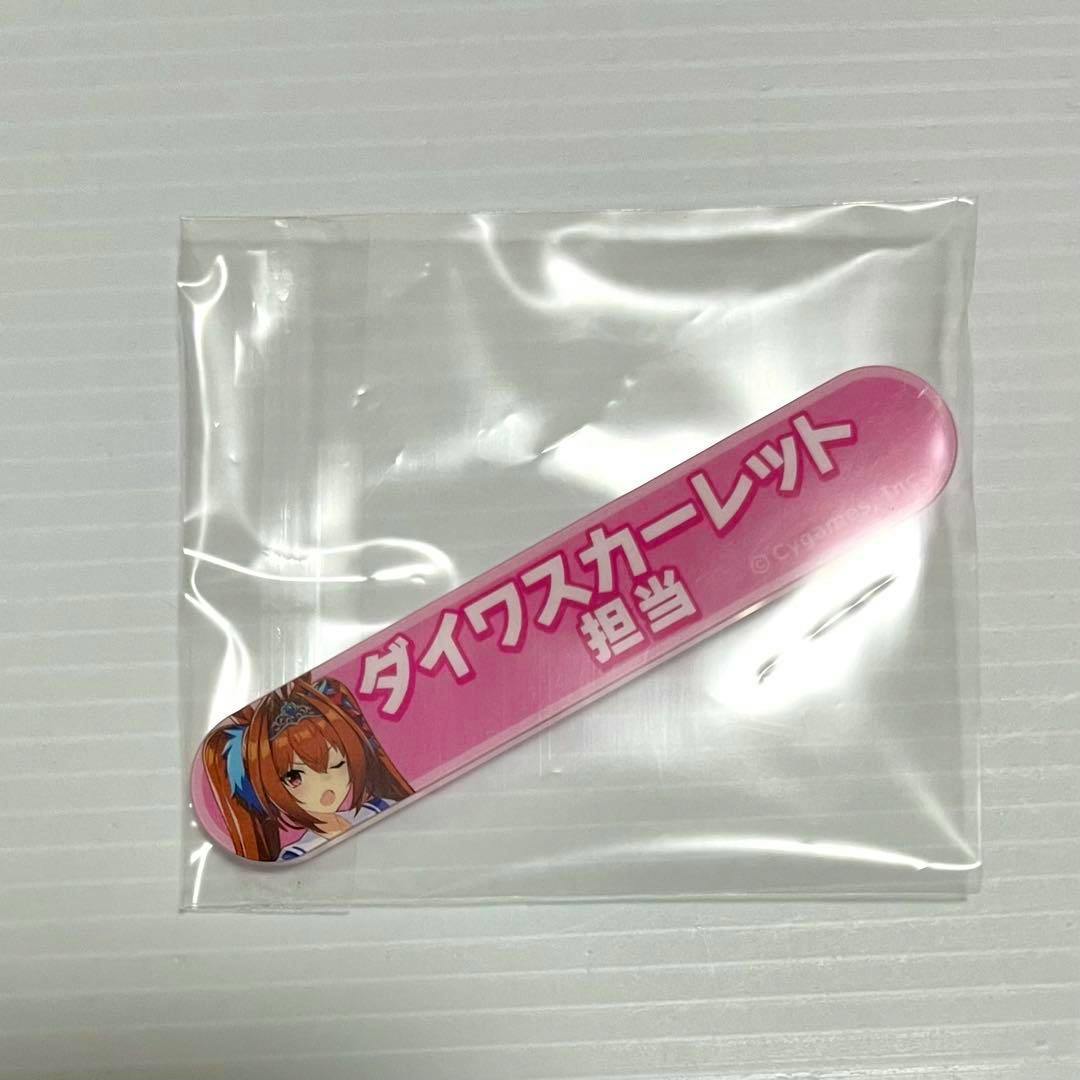 Pink acrylic badge reading “ダイワスカーレット 担当” with a small character illustration, inside a clear plastic bag on a white background.
