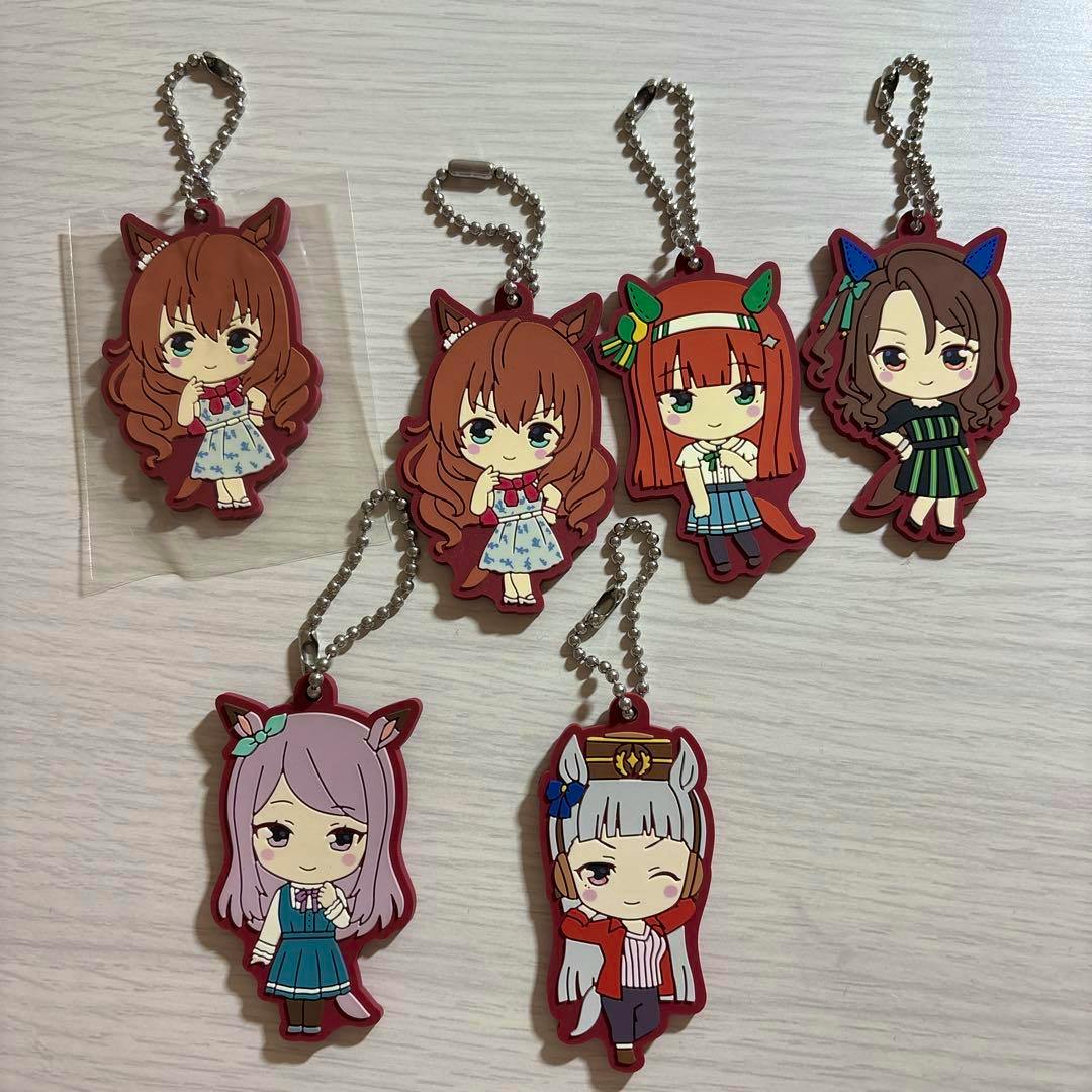 Six Uma Musume rubber strap keychains in casual outfits laid out on a light-colored wooden surface.