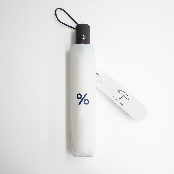 Folded white umbrella in its sleeve showing a '%' logo and an attached product tag.