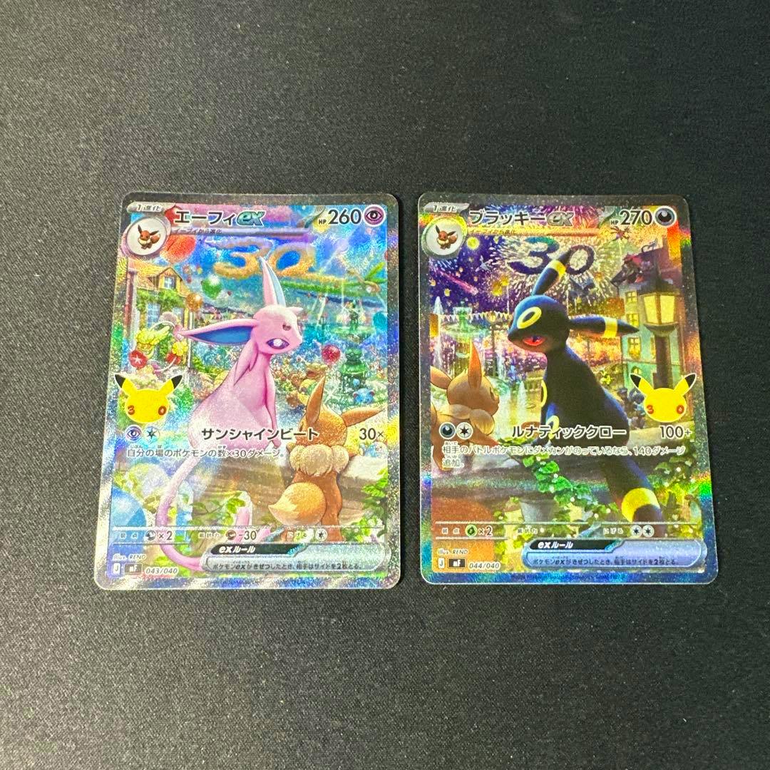 Two holographic Pokémon trading cards (エーフィex and ブラッキーex) displayed side-by-side on a dark textured surface.