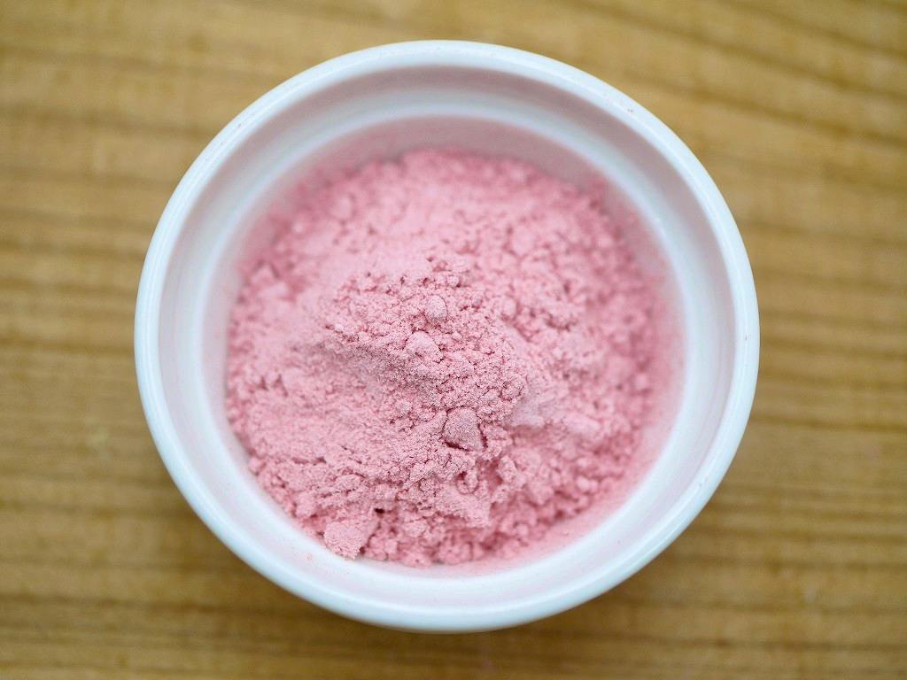 Top-down photo of pink ume (plum) powder in a white bowl on a wooden surface.