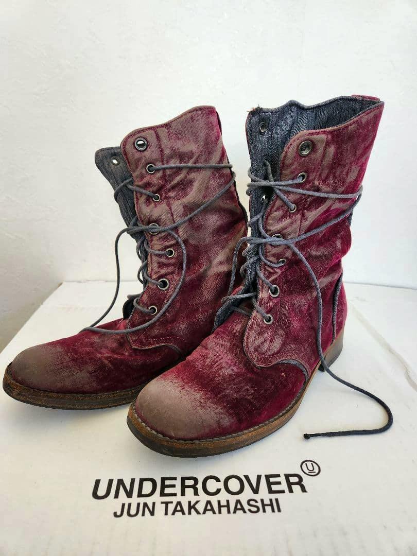 Pair of burgundy lace-up UNDERCOVER boots with a flocked finish displayed on a white box bearing the UNDERCOVER Jun Takahashi logo.