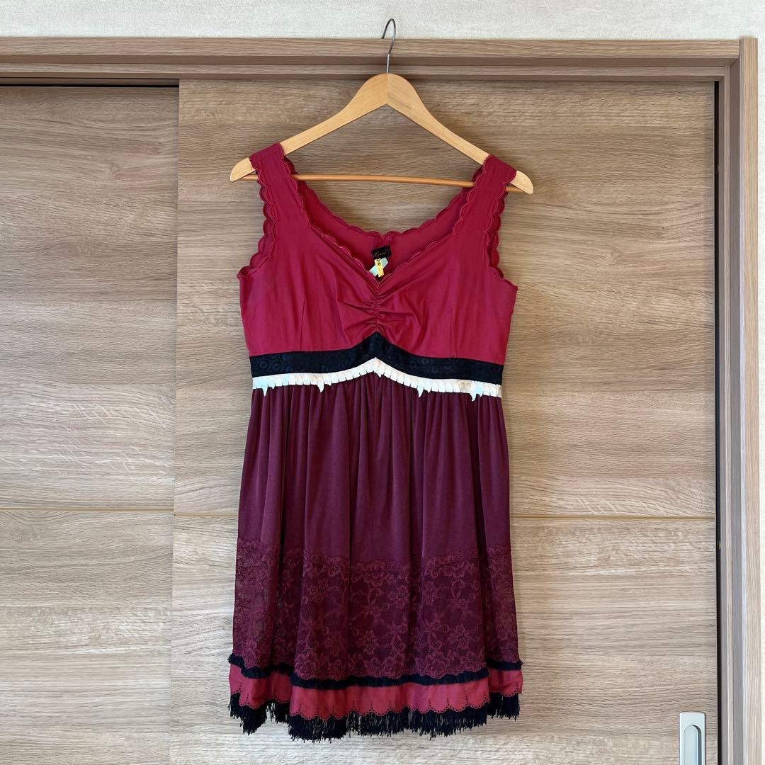 Burgundy sleeveless dress with a black-and-white waist band and lace-trimmed skirt hanging on a wooden hanger against a wood background.
