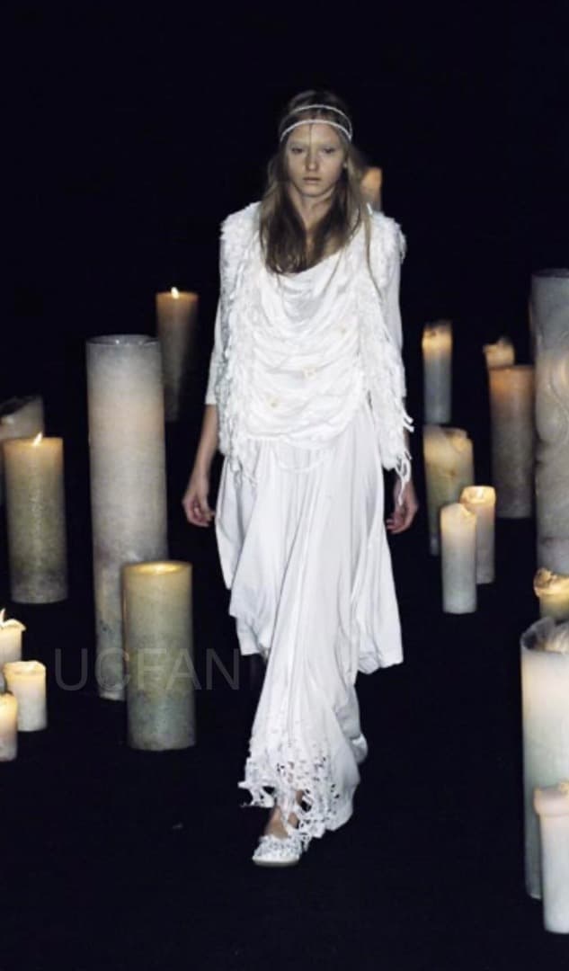 Runway model wearing the listed womens cotton BIG-T dress in white, photographed on a dark runway among lit candles.