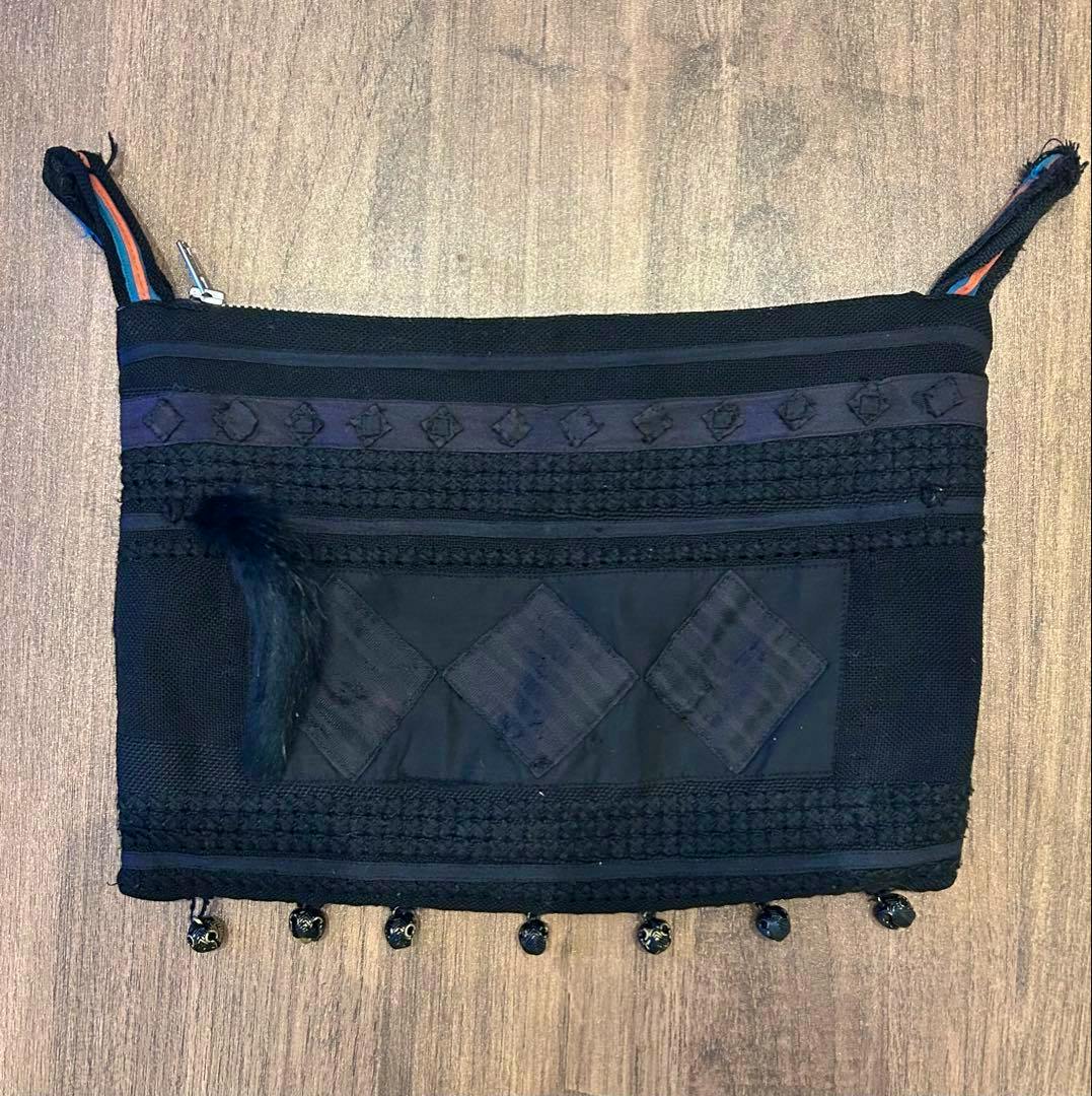 Front view of an undercover 2003 scab period black waist pouch laid flat, showing textured panels, diamond patchwork, small dangling beads along the bottom, and a short fur zipper pull.