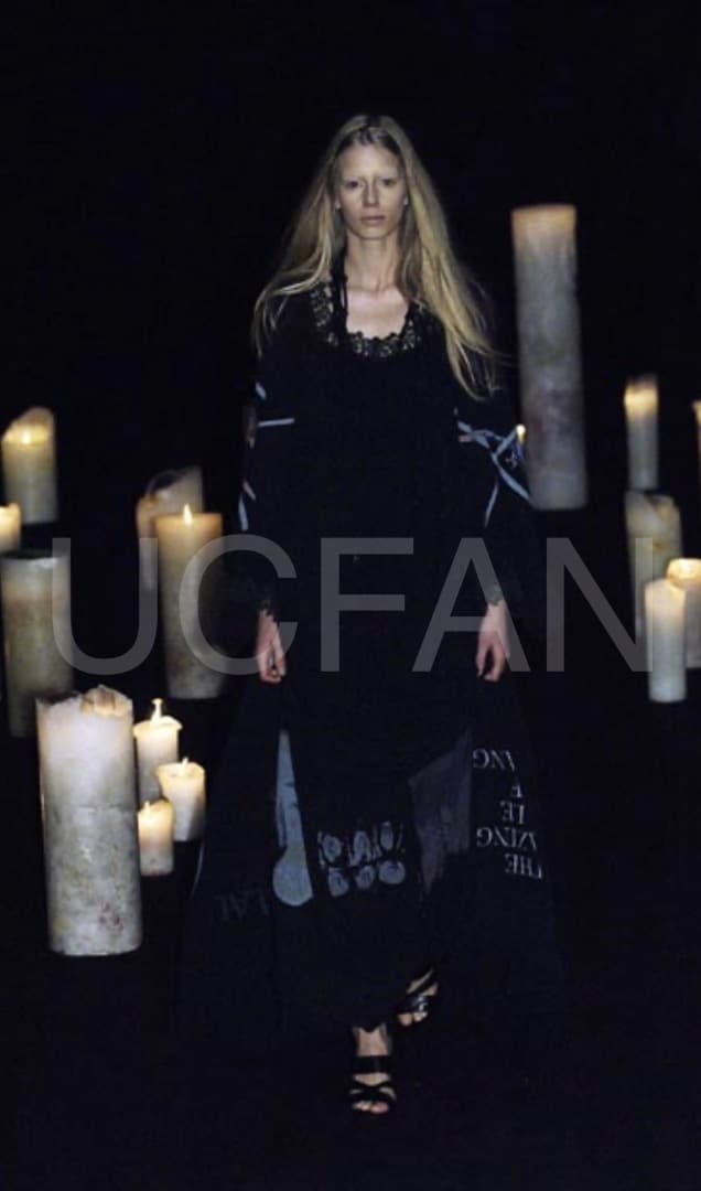 Runway photo showing a model wearing the listed UNDERCOVER pin-studded leather sandals, with lit candles in the background.
