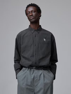 Male model wearing a black broad-check men's shirt tucked into grey trousers.