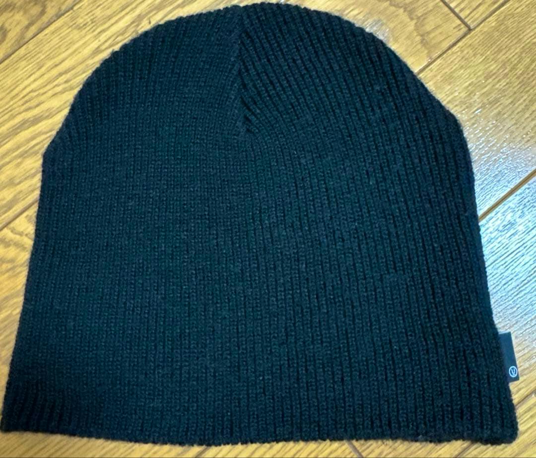 A black knit cap (beanie) laid flat on a wooden floor.