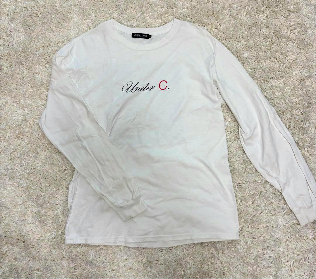 White UNDERCOVER long-sleeve T-shirt laid flat showing the front with a centered "Under C." chest print.
