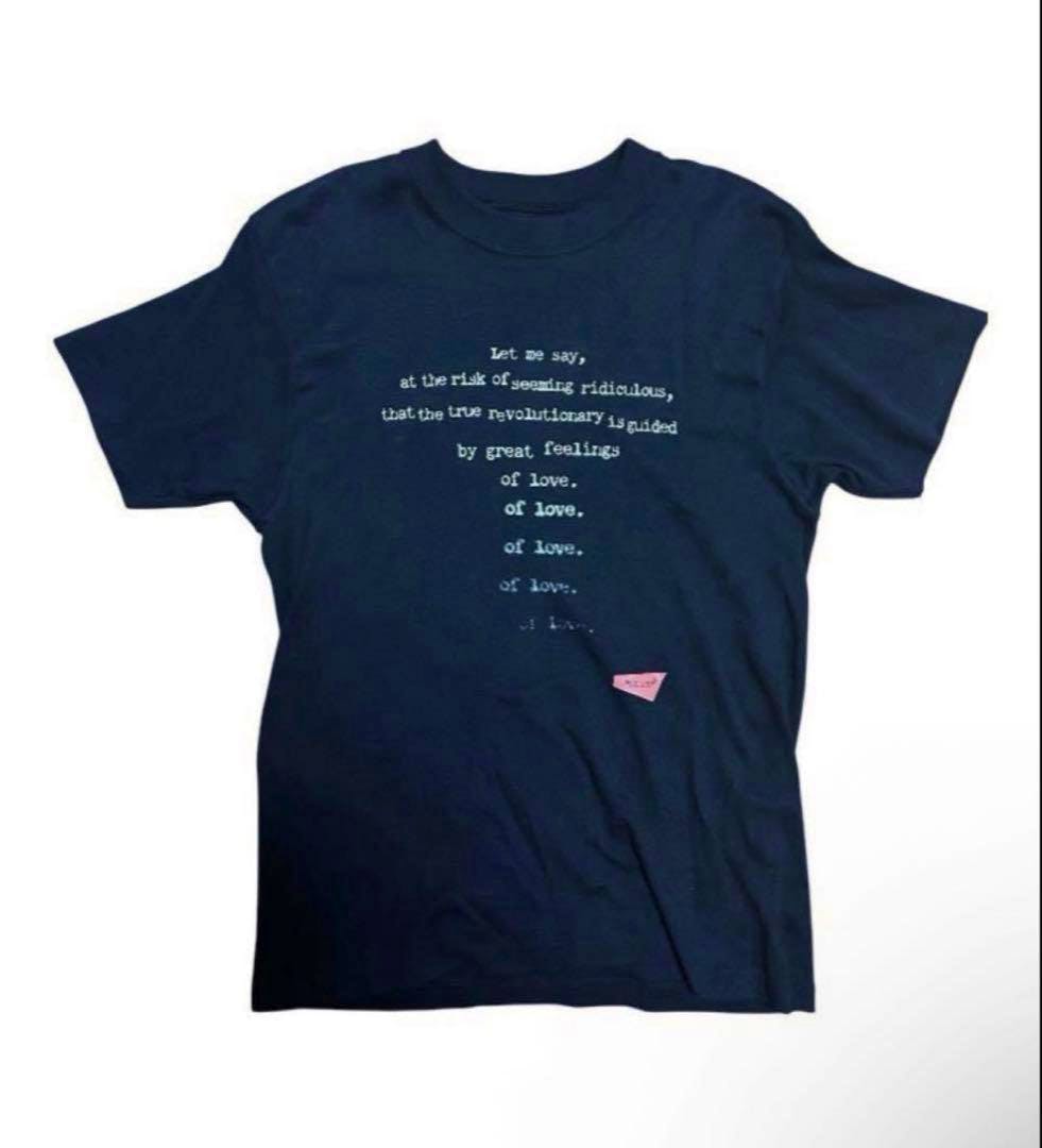 Front of a navy UNDERCOVER message t-shirt laid flat showing centered white printed text and a small pink label near the lower front.