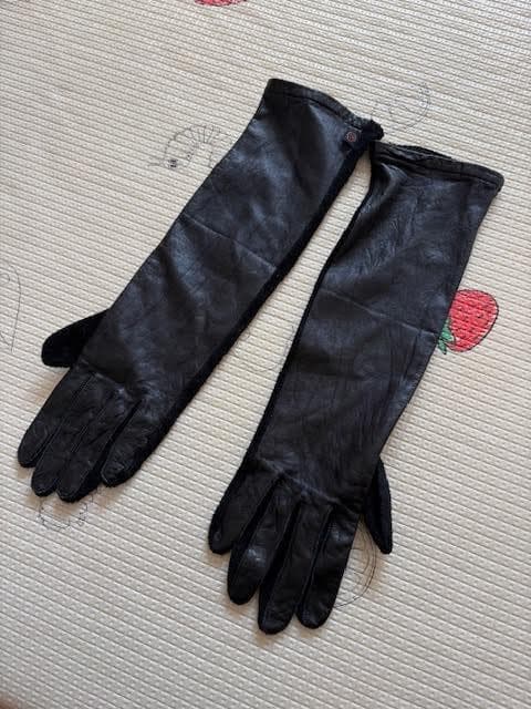 Long black women's suede leather gloves laid flat on a patterned mat, showing the exterior side.