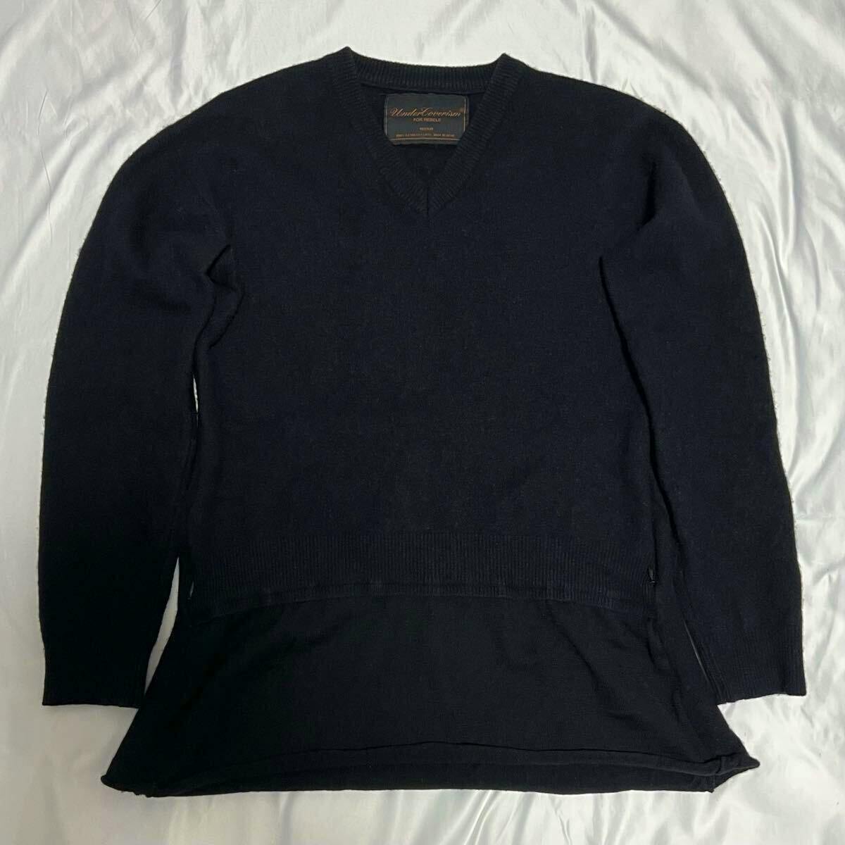 Black V-neck wool sweater laid flat on a white surface, showing the attached lower panel.