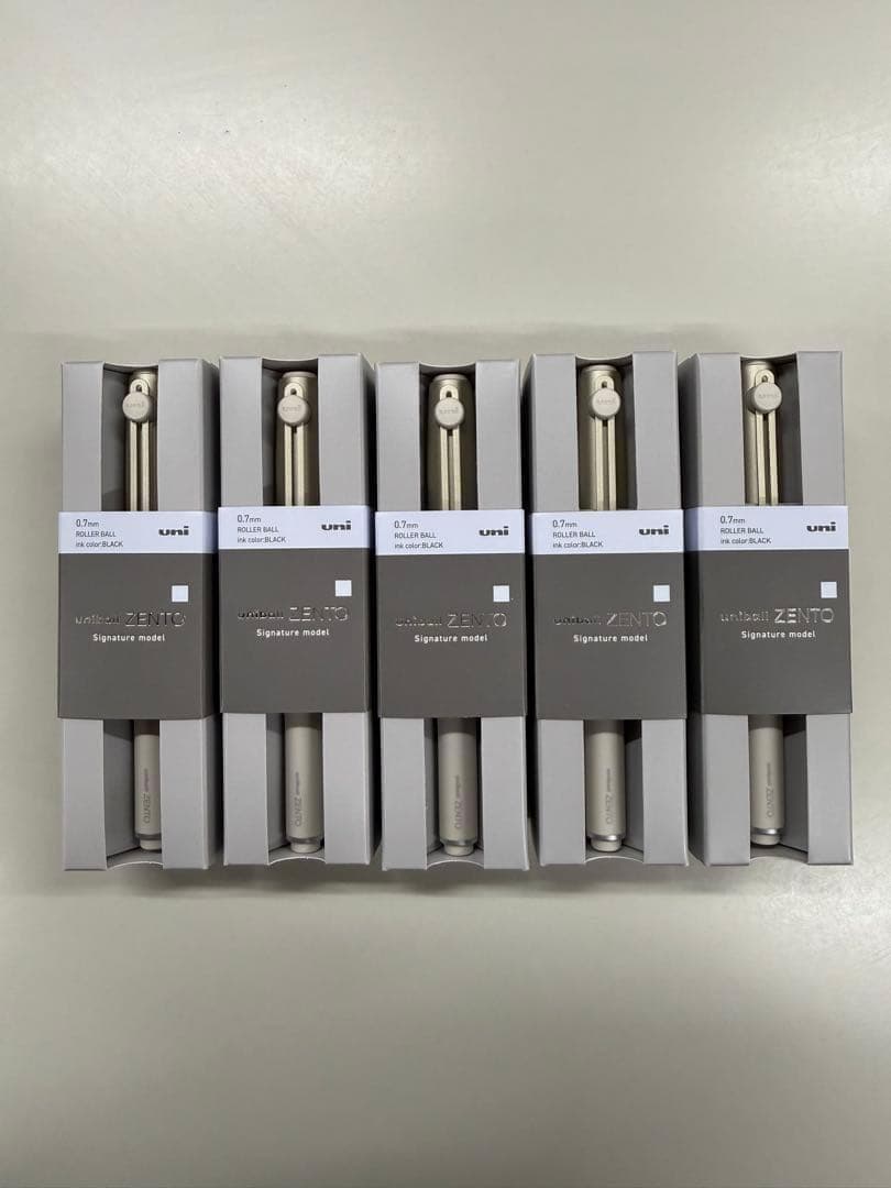 Five champagne gold ballpoint pens (uni ZENTO signature model) in their retail boxes arranged side-by-side.