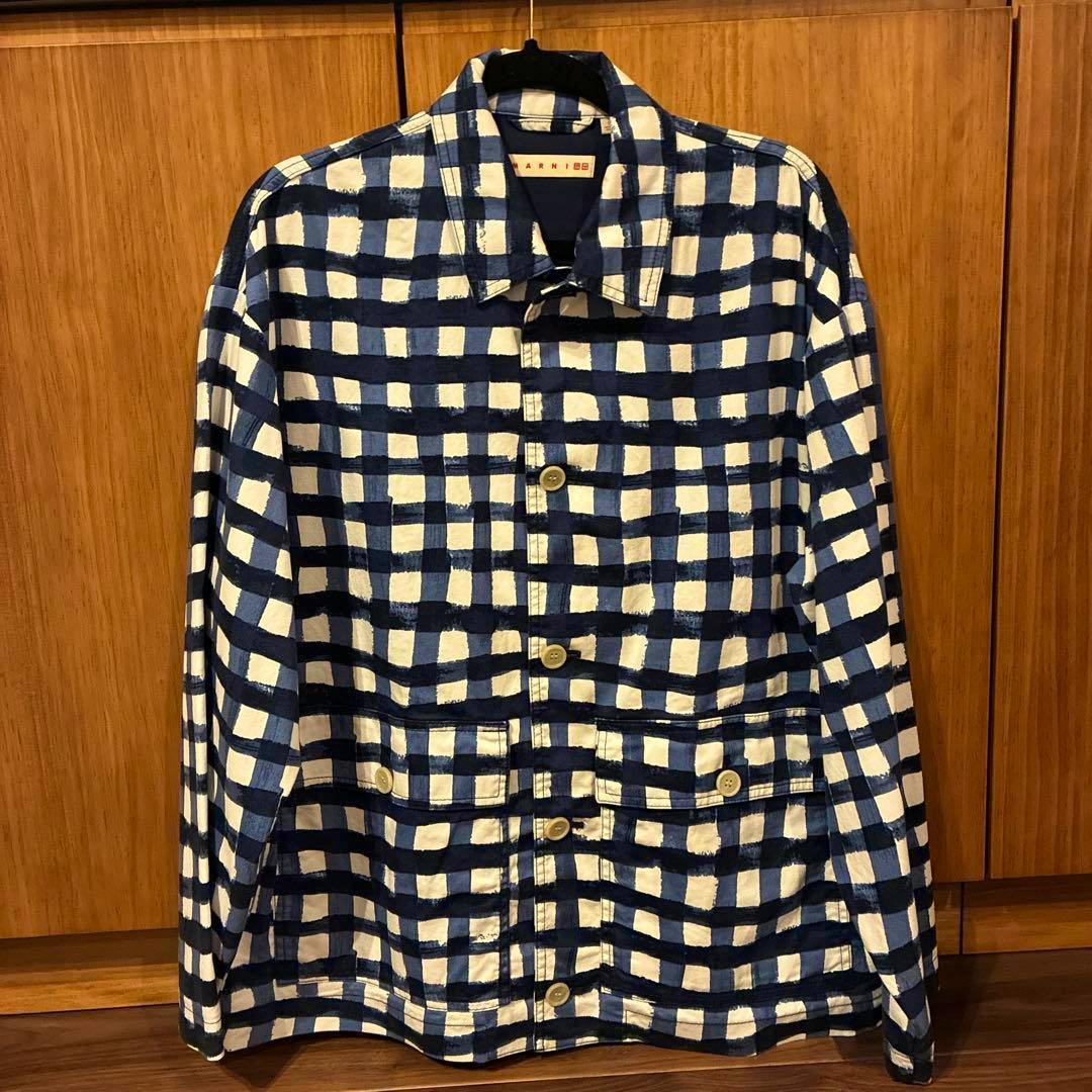 Front view of the UNIQLO and MARNI oversized utility men's cotton jacket in a blue-and-white check pattern hanging on a hanger.