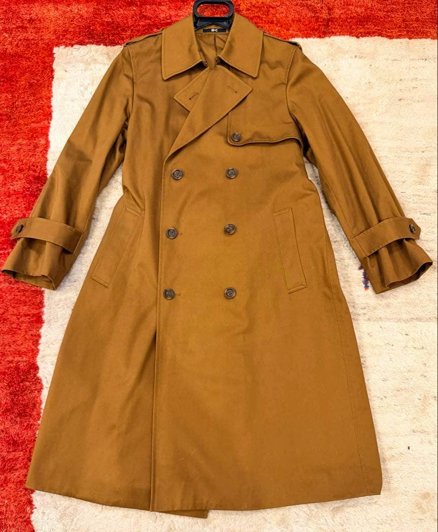 Front view of a brown Uniqlo women's cotton trench coat laid flat showing the double-breasted front, lapels, and buttoned sleeve straps.
