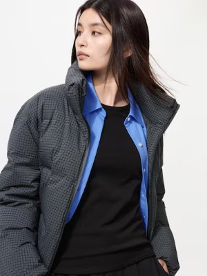 Woman wearing a black U-neck top visible under an open blue shirt and a gray jacket.