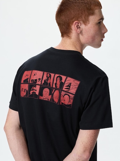 Male model wearing a black men's cotton T-shirt showing a red grid of NARUTO character portraits on the back.