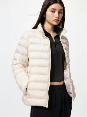 Woman modeling a light-colored women's padded jacket with hands in pockets, worn over a black top and black pants.