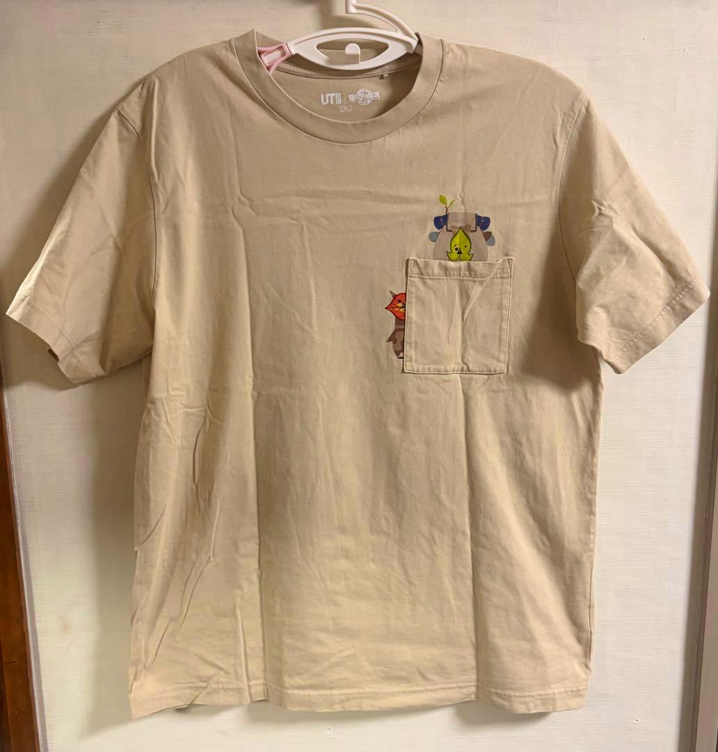 Front view of a beige UNIQLO 'ゼルダの伝説 ティアキン' pocket T-shirt on a hanger with small character prints near the chest pocket.