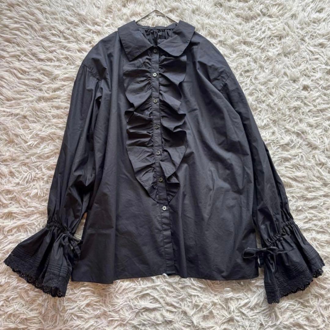 Black cotton women's blouse with a ruffled front and lace-trimmed frill sleeves laid flat on a rug.
